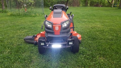 2007 Subaru Impreza - Orange Husqvarna riding lawn mower with front LED light bar and headlights on grass.