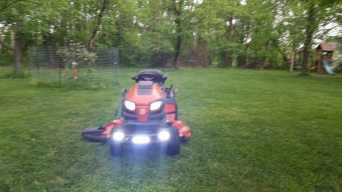 2007 Subaru Impreza - A red riding lawn mower with its headlights illuminated sits on a green lawn, with trees and a playground in the background.