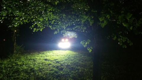 2007 Subaru Impreza - A vehicle's bright headlights illuminate a grassy area at night, viewed from under tree branches.