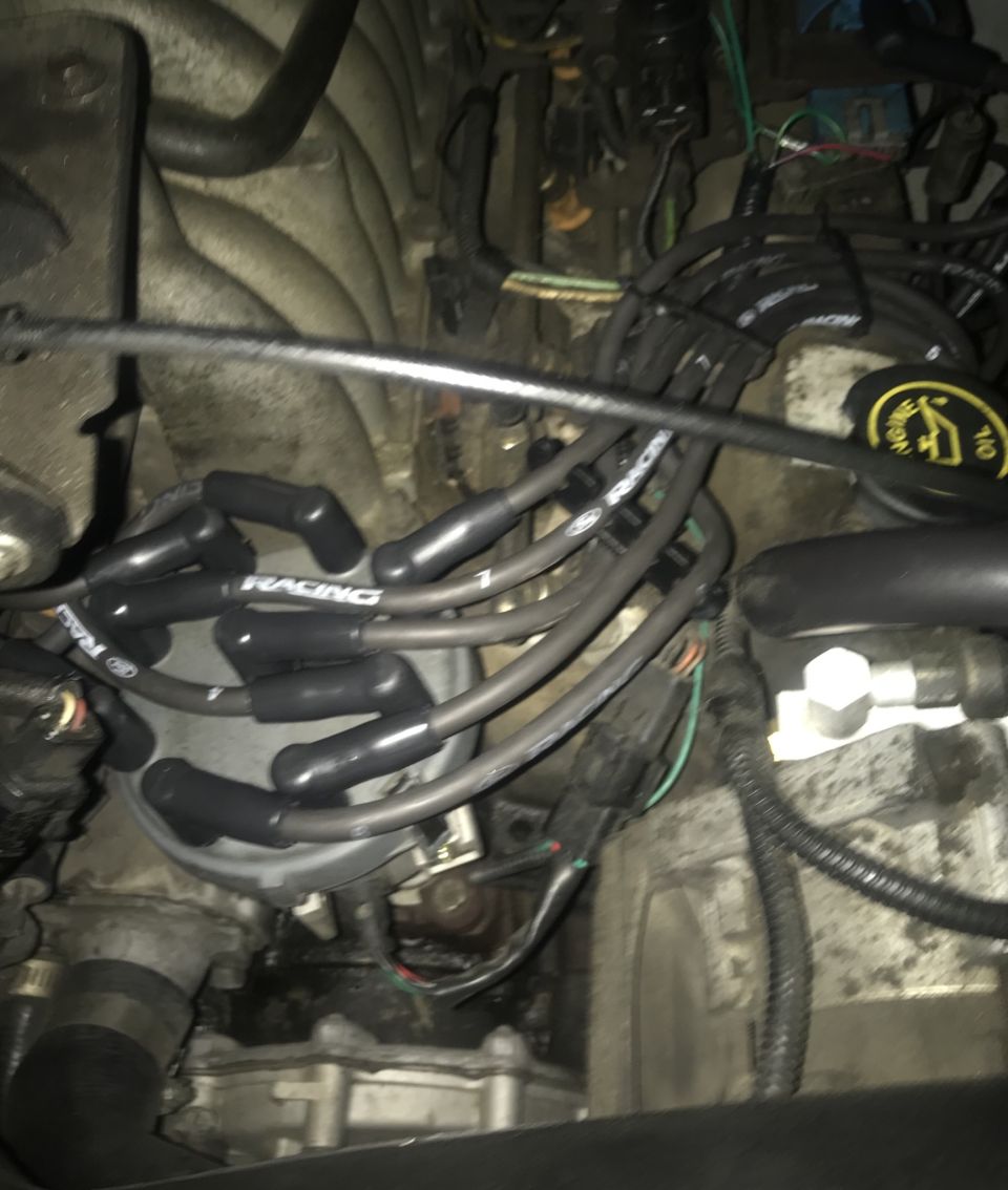 Engine compartment showing distributor cap, spark plug wires labeled 'RACING', and various hoses and connectors
