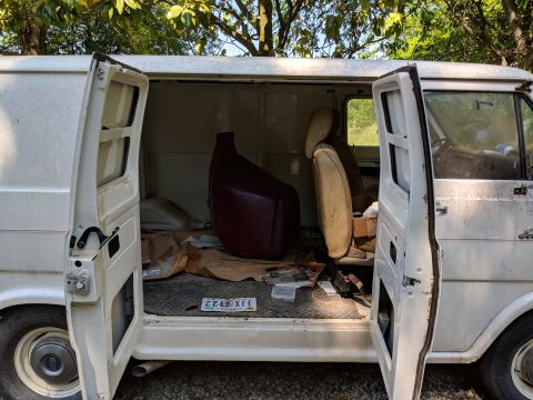 1971 Ford Ranchero - The interior of a white van is shown with its doors ajar, revealing seats and various items scattered on the floor.