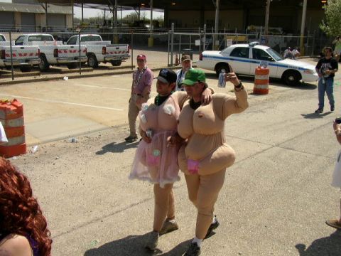 1995 Ford Bronco - Two individuals in humorous costumes are seen walking in a parking lot with several vehicles in the background.