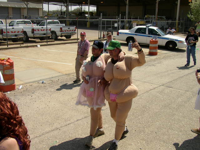 Two people in novelty costumes walk past parked trucks and a police car