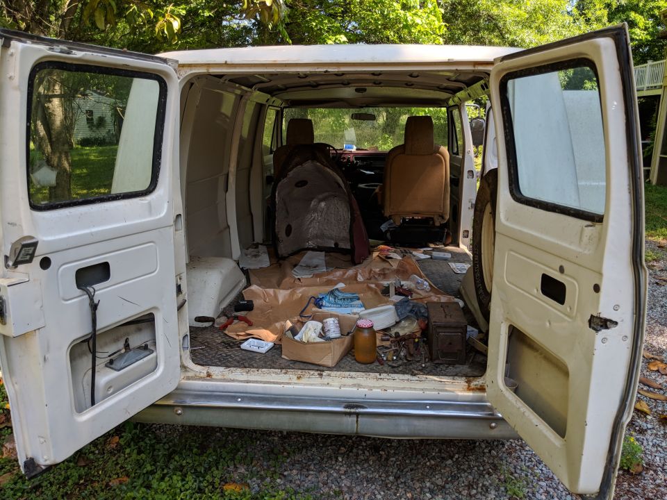 Open rear doors of a white van showing cluttered interior with seats and tools