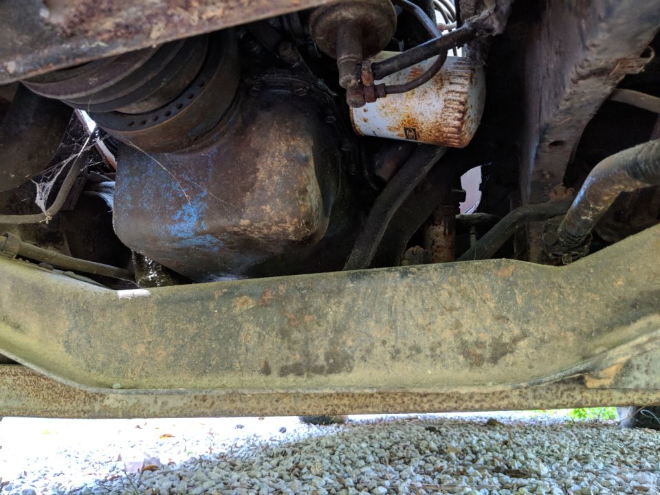 Underside view of engine oil pan and oil filter, with some rust and cobwebs
