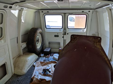 1971 Ford Ranchero - View inside a cargo van, including a spare tire and a large metal component. Other vehicles are seen through the windows.