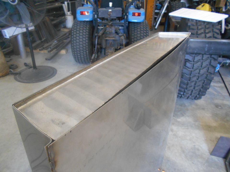 Metal box with visible welds, next to a blue tractor and a large tire