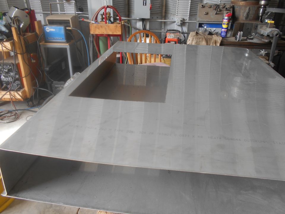 Metal sheet with a rectangular cutout, sitting on a workbench in a garage with tools and welding equipment in the background