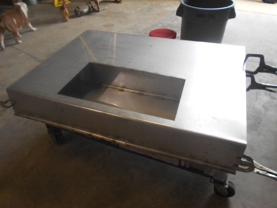 Metal fabrication on wheels with a rectangular cutout, viewed from a 3/4 front angle. A dog is in the background