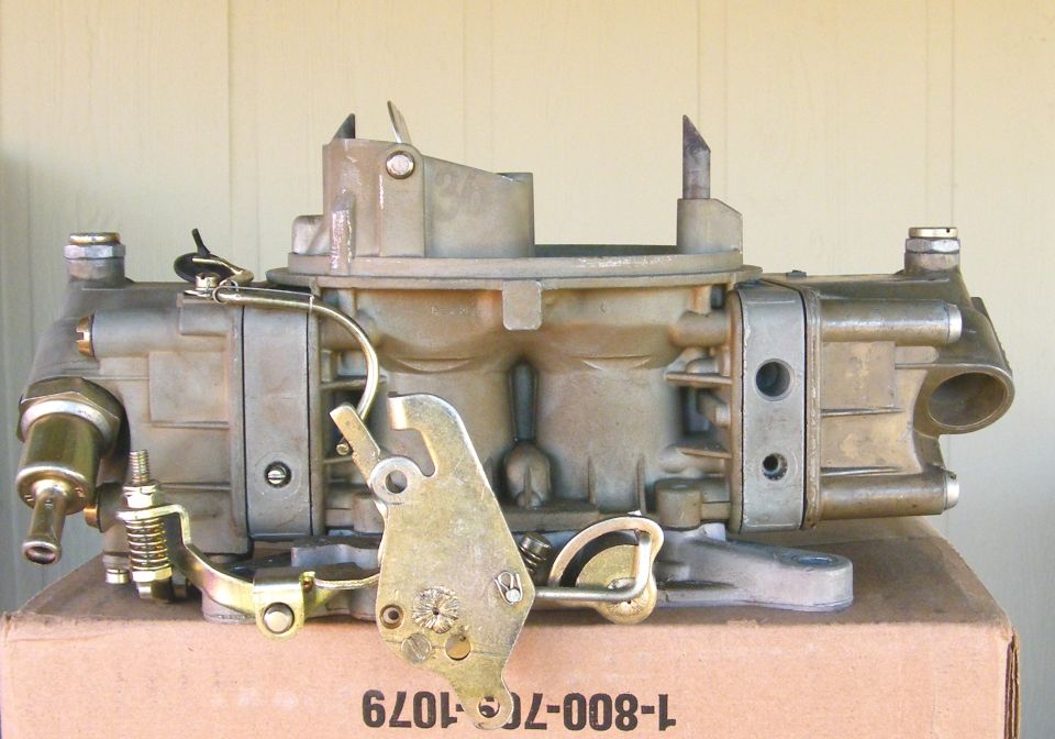 Side view of a rebuilt Holley four-barrel carburetor with linkage on yellow surface