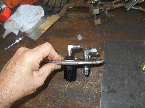1992 Ford Bronco - A hand holds a metal fuel pump assembly with angled fittings and a black central component on a workbench.