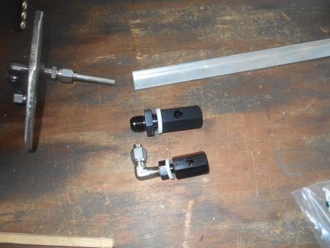 1992 Ford Bronco - Various metal fittings and a piece of aluminum extrusion are laid out on a wooden surface, with the Supermotors.net logo in the lower right…