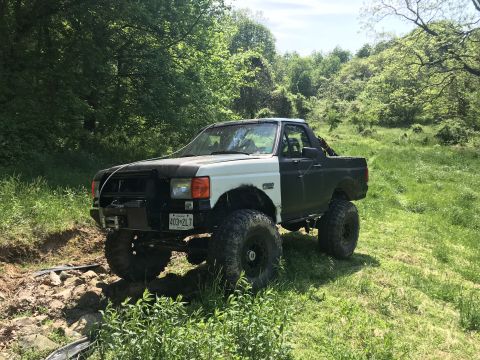 1989 Ford Bronco - A modified 1989 Ford Bronco sits in a grassy, wooded area with its front end on a rocky path.