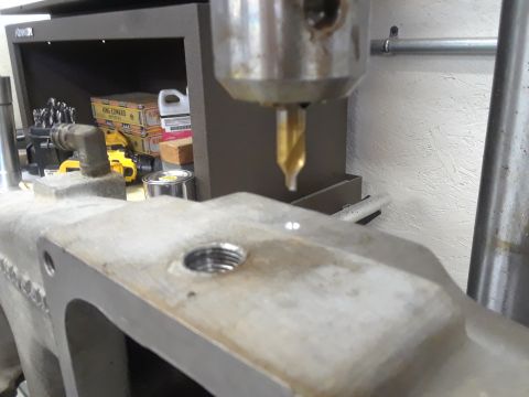 1985 Ford Bronco - Drilling a hole in an engine part with a drill press. Tools and supplies are visible on a shelf in the background.