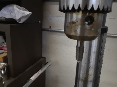 1985 Ford Bronco - Close-up of a drill press chuck holding a tap, with a rag visible on a shelf.
