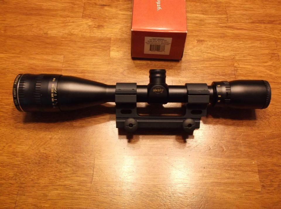 Black rifle scope with a red box on a wooden surface. The scope has a Swift logo