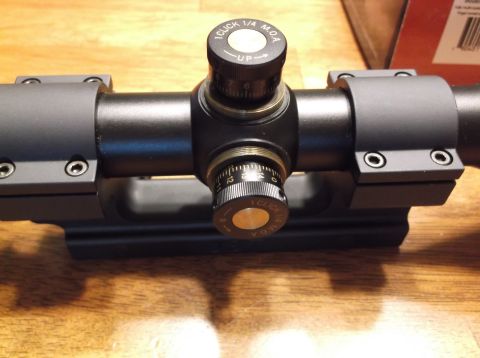 1995 Mercury Grand Marquis - Close-up of a rifle scope's adjustment turrets, showing MOA markings and an indicator for upward adjustment.