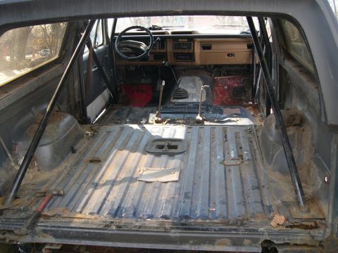 1986 Ford Bronco - Interior of a stripped-down SUV, likely from the 1980s, with a roll cage installed.