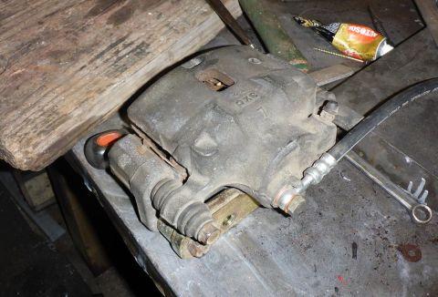 1969 MINI Cooper - A single brake caliper, likely from a vehicle, is shown on a workbench with various tools and debris.