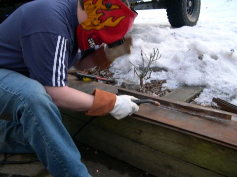 1986 Ford Bronco - A person welds a metal piece outdoors in the snow, with a vehicle tire visible in the background.