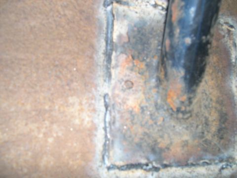 1986 Ford Bronco - Detail of rusted metal and a black pipe, possibly from a vehicle's frame or body panel.