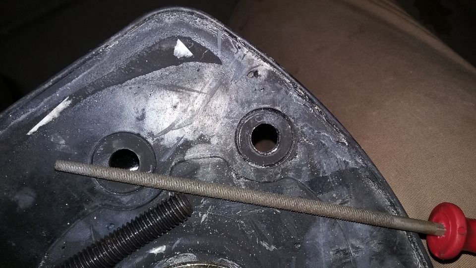 Close-up of a black plastic automotive part being filed, with a threaded bolt visible