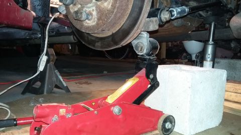 2000 Pontiac Grand Prix - The rear suspension and brake assembly of a vehicle is supported by jack stands and a hydraulic jack, indicating maintenance or repair work.