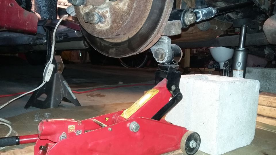 Rear suspension and brake assembly on jack stands with a red hydraulic jack
