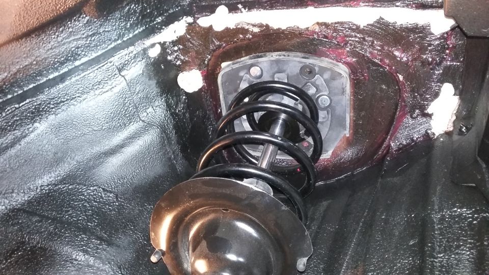 Close-up of a car's front strut assembly with black coil spring and metal mount