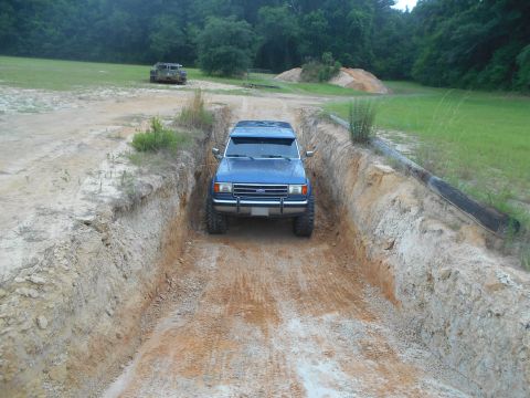 1992 Ford Bronco - A blue SUV navigates a narrow dirt path with steep sides, while another vehicle sits in the distance.