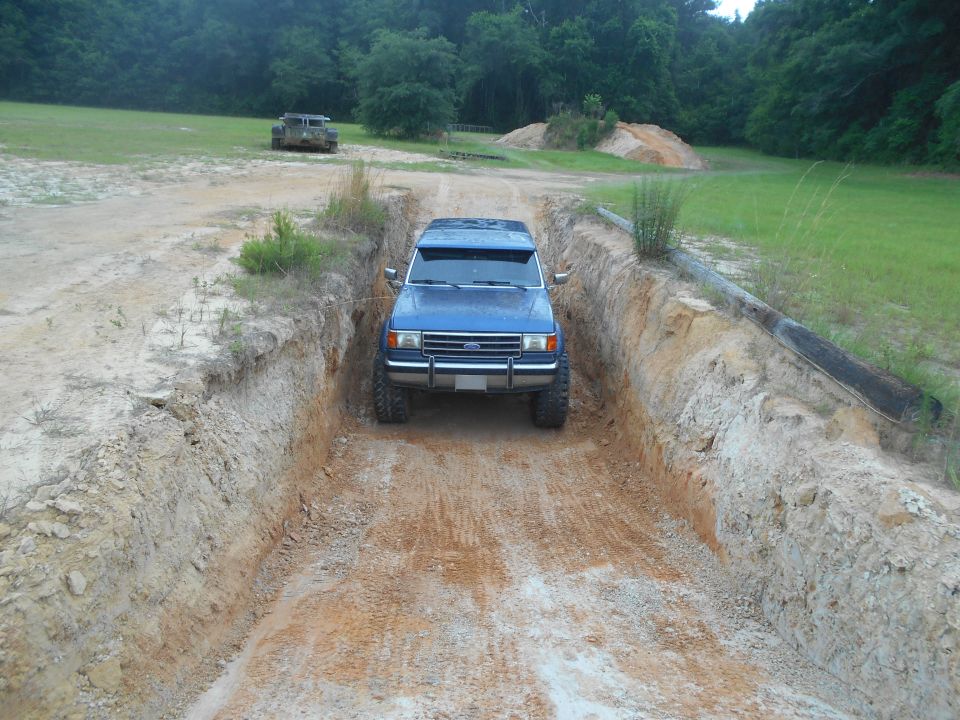 Blue SUV driving down a dirt ditch. Another vehicle is visible in the background