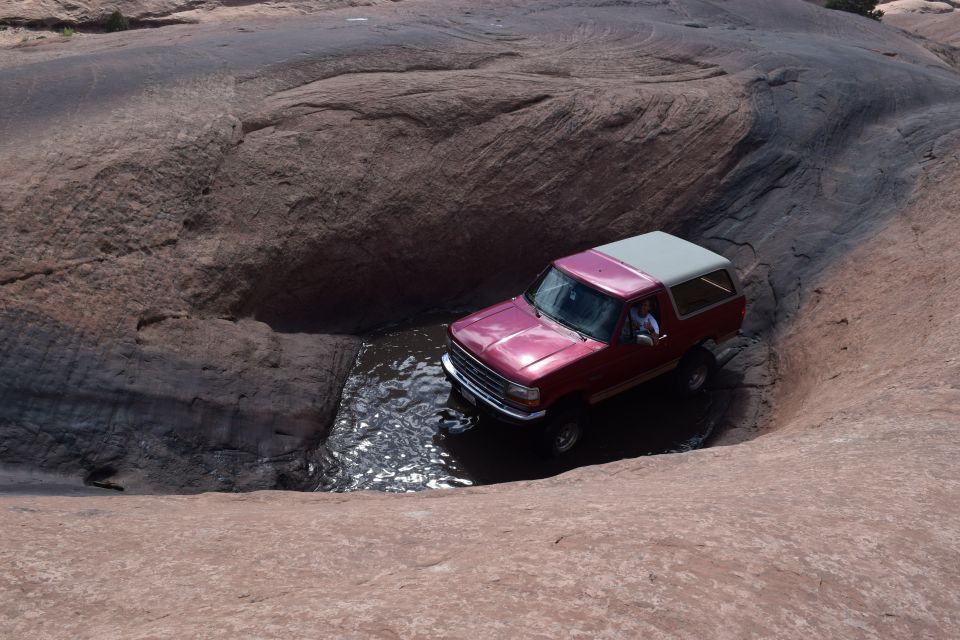 Red 1995 Ford Bronco navigating water in a rocky desert landscape