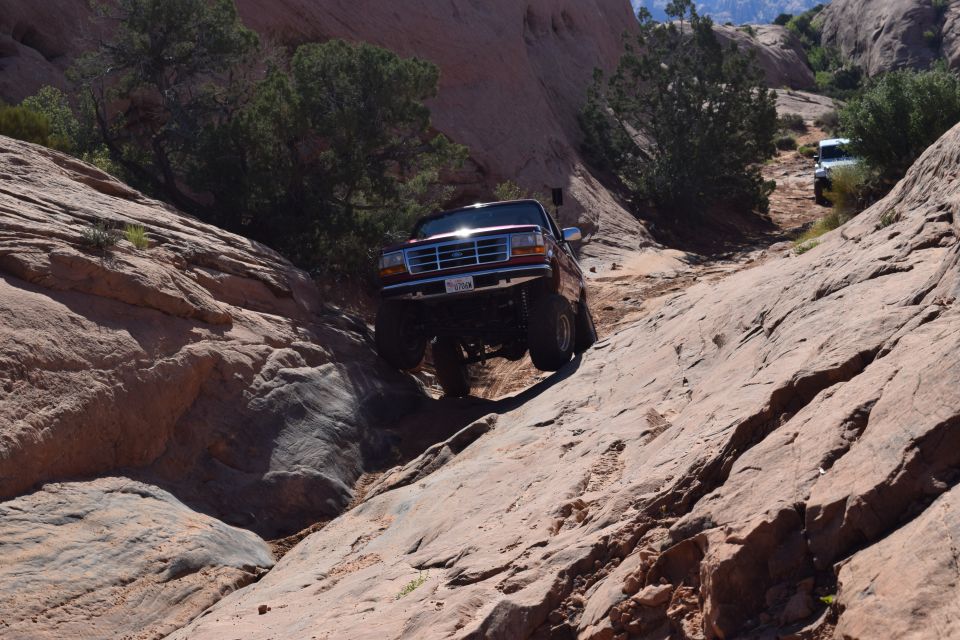 1995 Ford Bronco navigating a steep, rocky off-road trail with another vehicle visible in the distance