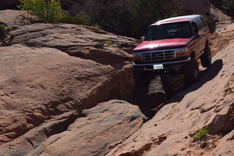 1995 Ford Bronco - A red Ford Bronco tackles a challenging off-road course in a desert landscape.