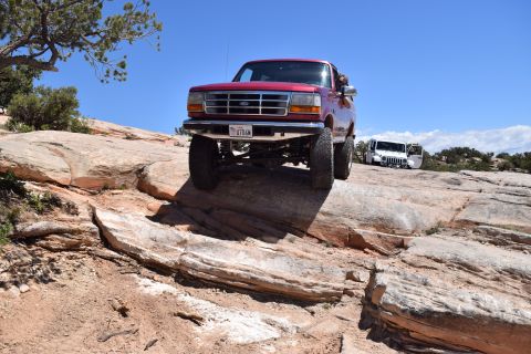 1995 Ford Bronco - A red 1995 Ford Bronco navigates a rocky trail, with another vehicle visible in the distance.