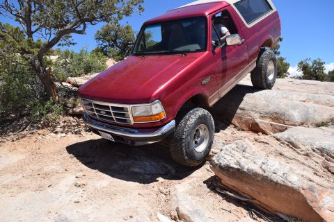 1995 Ford Bronco - Red 1995 Ford Bronco navigating rocky terrain during an off-road excursion.