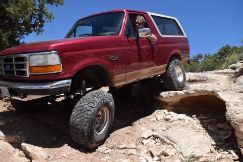 1995 Ford Bronco - A red Ford Bronco navigates a challenging off-road course under a clear blue sky.