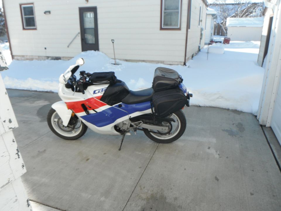 White, blue and red Honda CBR sportbike with black tank bag and saddlebags parked on a snowy driveway