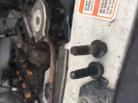 1996 Ford Bronco - Close-up of bolts and warning labels in a vehicle's engine bay.