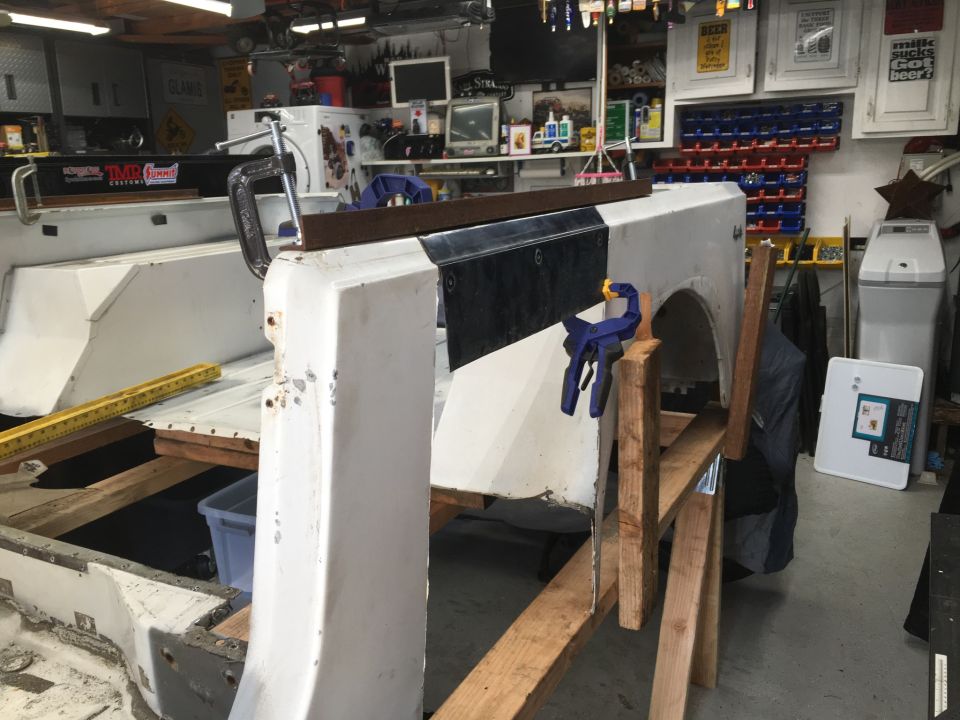 White Jeep body panel clamped to wooden supports during repair in a garage