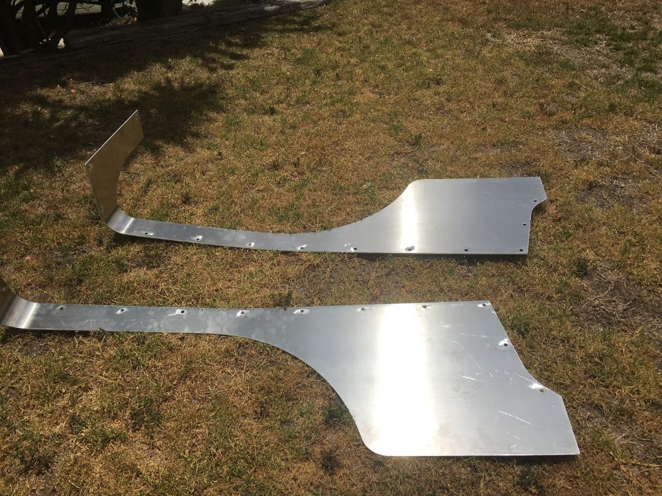 Two aluminum body panels with pre-drilled holes laid on grass