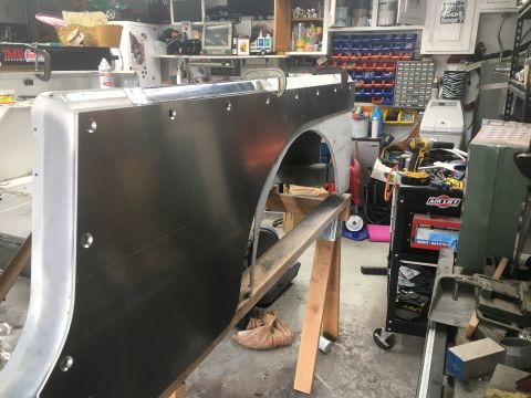 1992 Jeep Wrangler - A bare metal Jeep Wrangler fender panel is mounted on sawhorses in a cluttered garage, ready for bodywork.