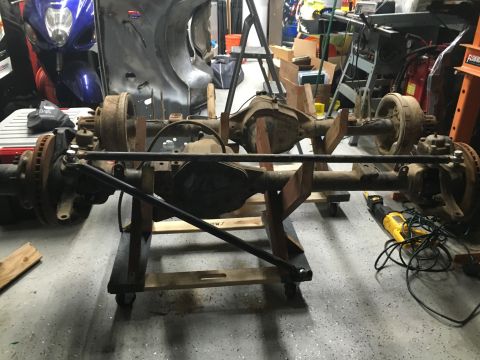 1992 Jeep Wrangler - Two vehicle axles are mounted on a wooden stand in a workshop setting. A yellow saw lies on the floor nearby.