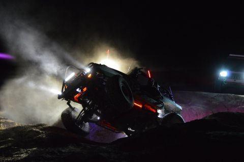 1992 Jeep Wrangler - This off-road buggy, illuminated by bright lights and neon accents, navigates challenging terrain in the dark, with another vehicle visible…