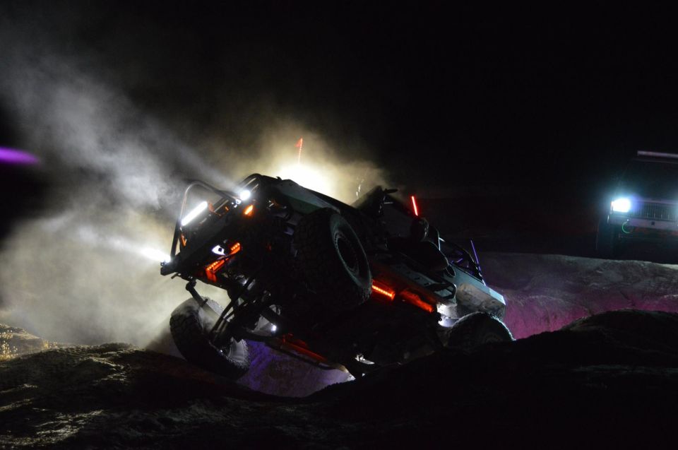 Off-road buggy with bright lights and neon accents navigates rough terrain at night