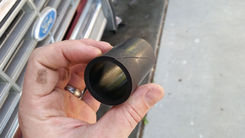 Hand holding a black rubber hose section. Ford grille visible in background