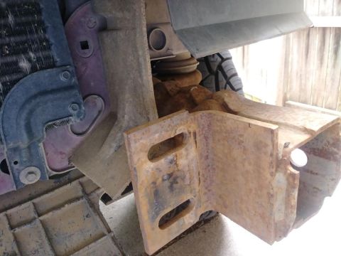 1996 Ford Bronco - Close-up of a heavily rusted bumper bracket on a 1996 Ford Bronco, showing mounting hardware and a portion of the radiator.
