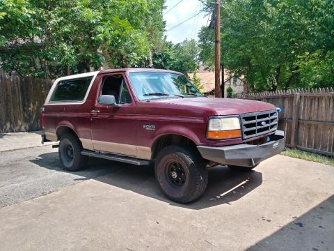 1996 Ford Bronco - This maroon Ford Bronco is parked outside on a paved surface with a wooden fence in the background.