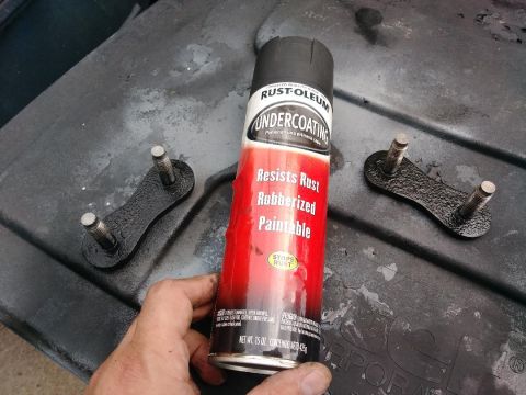 1996 Ford Bronco - A can of Rust-Oleum Undercoating sits next to two metal brackets with bolts, likely for a vehicle repair or modification.