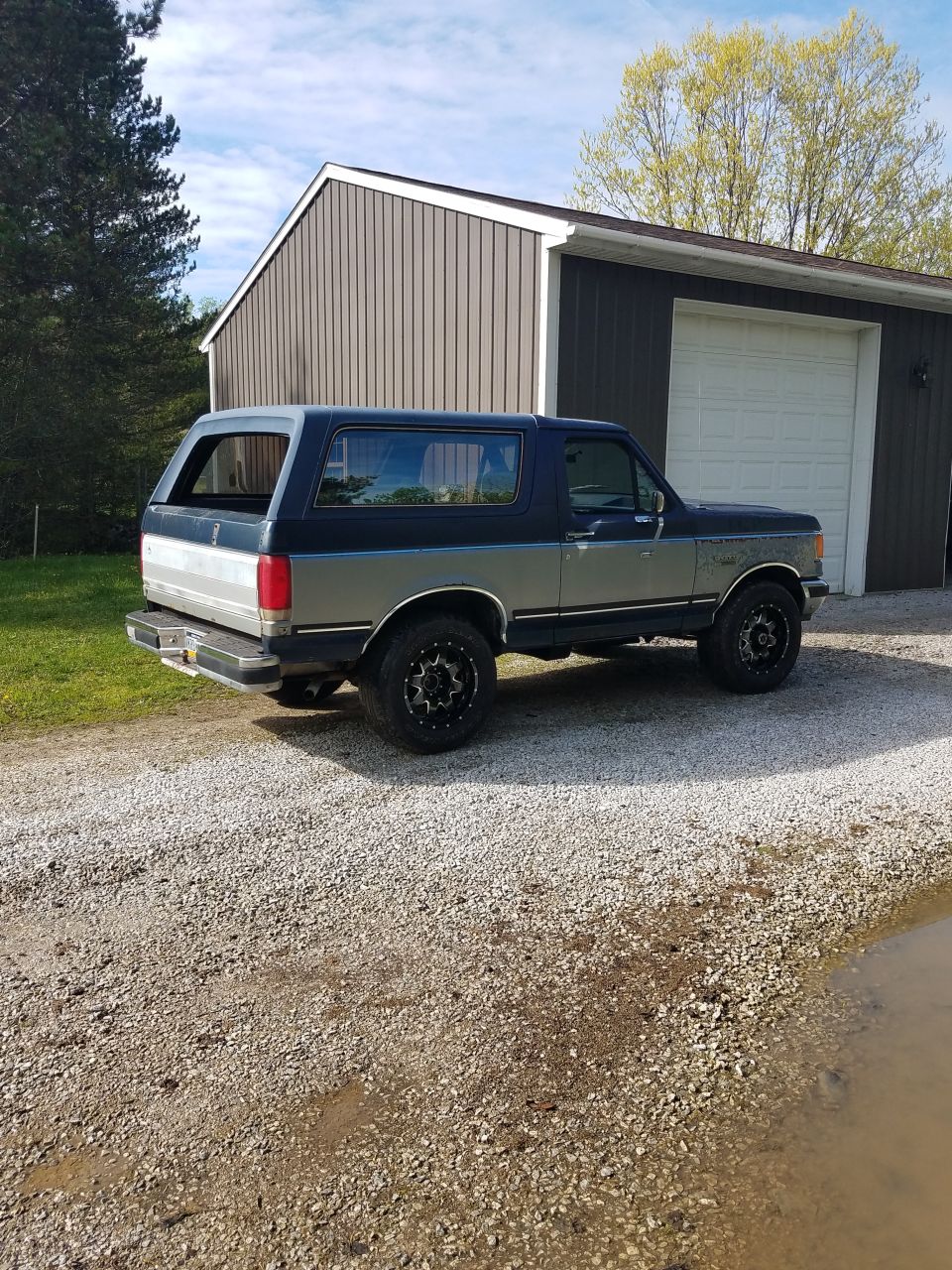 Dark blue and silver two-tone 1987 Ford Bronco parked in gravel driveway